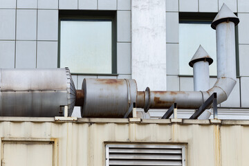 Wall of a building, industrial pipes, windows in the background.