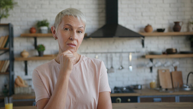 Elderly pensive woman thoughtfully at idea hold hand to chin with puzzled facial expression