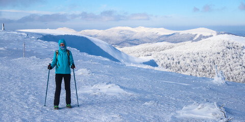 hiker girl stands in mountain glade admiring panorama of snowy mountains with frozen vegetation