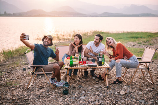 Group of diversity friends enjoy camping and make a selfie with beautiful sunset view at the lake - Travel on vacation concept