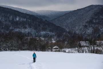 Hiker girl walks along snowy field with mighty mountains in background; hiking in cold winter weather