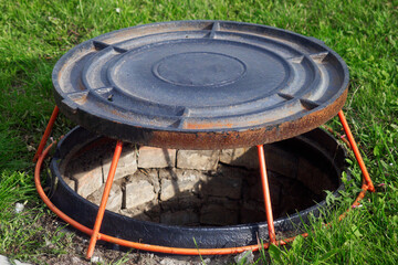 Open well hatch on green lawn. Manhole cover is on stand. Device for ventilation of wells..