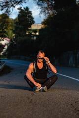 Handsome male backpacker resting on a asphalt road on a sunset. Hiking, exploring the nature concept