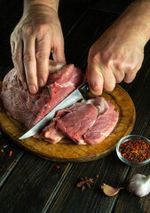 Cook's hands cut with a knife raw beef steak on a wooden cutting board. The concept of the process of cooking a meat dish with aromatic spices