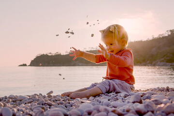 Rest on the sunset sea. A cute child throws pebbles and has fun. Little girl is playing on the seashore