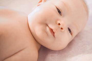 Portrait of small cute girl in her cozy white bed. Portrait of adorable smiling newborn child. Baby girl lying on the bed. Beautiful smiling cute kid. A small baby in a good mood