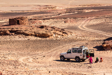 Sinai peninsula, Egypt - January 2022: Car and local girls in Sinai desert near Navamis, a complex of stone structures. Yellow and orange sandstone textured carved mountain. Egyptian desert landscape