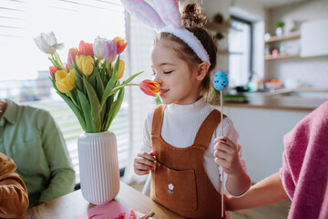 Little girl smelling bouquet of tulip flowers during decorating easter eggs with her family.