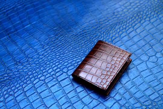 A unisex bifold cardholder cum minimalist wallet made with pure leather and in brown color, contrasting with the background of blue crocodile leather.
