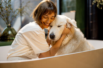 Portrait of a young woman with her cute dog in bathtub. Woman hugs with pet before washing. Concept...