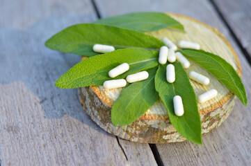 Leaves and flowers of medicinal sage lie on a wooden table next to homeopathic pills, herbal medicine, alternative medicine.