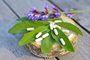 Leaves and flowers of medicinal sage lie on a wooden table next to homeopathic pills, herbal medicine, alternative medicine.