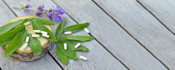 Leaves and flowers of medicinal sage lie on a wooden table next to homeopathic pills, herbal medicine, alternative medicine.