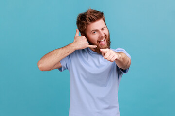 Man flirting and pointing at camera with attractive smile, making call me gesture with fingers.