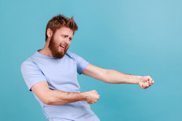 Man in blue T-shirt pretending to pull invisible rope, holding something heavy.