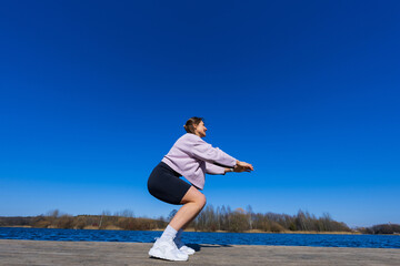Fototapeta premium A young athletic woman squats during a workout.The shooting point from below. View of the pond