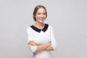 Woman standing with crossed arms, looking at camera with toothy smile, expressing positive emotions.