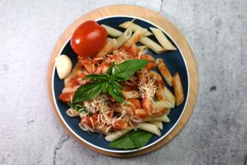 pasta in tomato sauce with basil leaf on a plate on a wooden tray