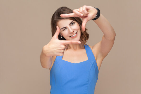 Woman making frame gesture, finding perfect angle, winking eye and smiles broadly.