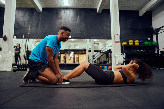 Mixed race friends doing cross fit in the gym. African American male encouraging African American female during sit-ups. High quality photo