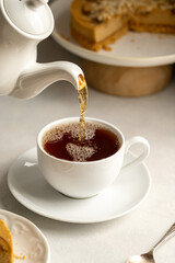 Pouring hot tea in white, ceramic cup, served with cake