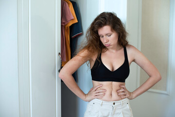 Unhappy sad upset young woman with fat on her stomach, girl worried about body fat touching her...