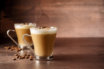Two cups of coffee hot drinks, with milk foam in glass cups, over wooden background, copy space