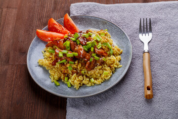 Chicken rice in teriyaki sauce garnished with green onions on a wooden table next to soy sauce on the table on a napkin next to a fork.
