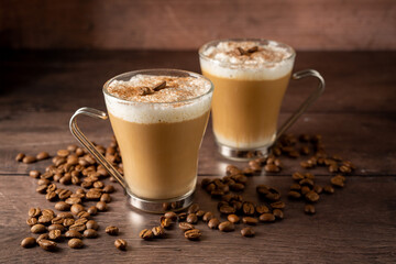 Two cups of coffee hot drinks, with milk foam in glass cups, over wooden background