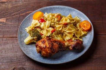 Pasta with vegetables and cherry tomatoes with baked chicken leg on the table