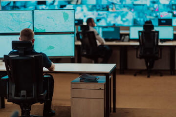 Group of Security data center operators working in a CCTV monitoring room looking on multiple...