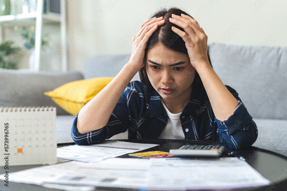 Wall mural Business financial concept, owe asian young woman, female sitting expression face stressed by calculate expense on table from invoice or bill, have no money to pay mortgage or loan. Debt, bankruptcy.