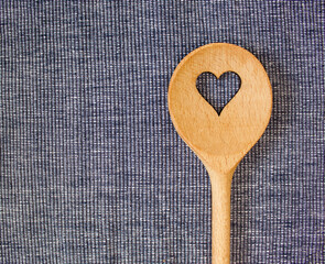 wooden spoon with a heart cutout on a blue and white doily, lying on the right side, close up, top view, copy space