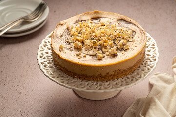 Whole caramel cheesecake on cake stand, neutral warm background