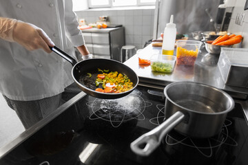cooking food, profession and people concept - close up of male chef with frying pan stewing vegetables at restaurant kitchen