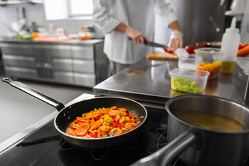 cooking food, profession and people concept - close up of frying pan with stewing vegetables and male chef at restaurant kitchen