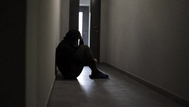 Silhouette of a depressed man sitting on the walkway of an apartment building. Sad man, crying, drama, lonely and unhappy concept.