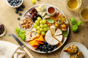 Cheese platter with fruits, nuts and snacks. Warm background. Top view.