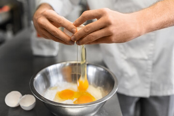 cooking food, baking and people concept - close up of male chef cook with flour breaking eggs into...