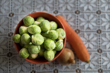 Brussels sprouts in a clay pot, next to onions and carrots, healthy vegetables.