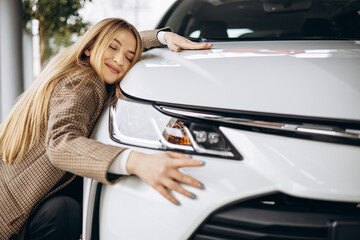 Beautiful woman hugging a car in a car showroom