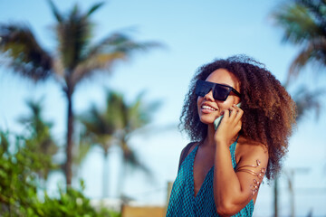 young brazilian black girl with afro hairstyle talking on the cell phone on the beach with palm...
