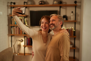 Cheerful mature couple taking selfie with smart phone at home