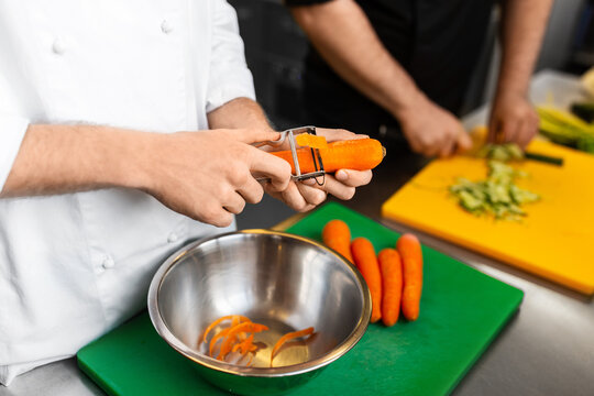 cooking food, profession and people concept - close up of male chef cook with knife peeling carrot at restaurant kitchen - Powered by Adobe