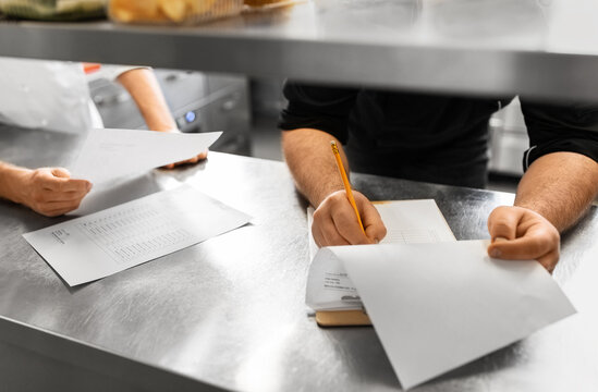 restaurant business, profession and people concept - close up of male chef with clipboard and bills filling papers on kitchen - Powered by Adobe