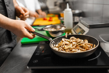 cooking food, profession and people concept - close up of male chef with frying pan stewing champignons at restaurant kitchen