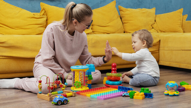 A young mother plays educational games with her baby at home on the floor