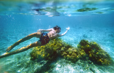 Fototapeta na wymiar Diving teenage boy snorkeling over the coral reefs underwater photo in the clean turquoise lagoon on Le Morne palm trees beach with Le Morne Brabant mount. Mauritius island. Exotic traveling concept