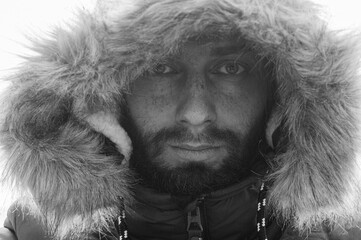 Bearded young man with freckles in a winter jacket with fur