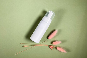 above view of closed white blank pump plastic bottle and natural dried pink spikelets on khaki...